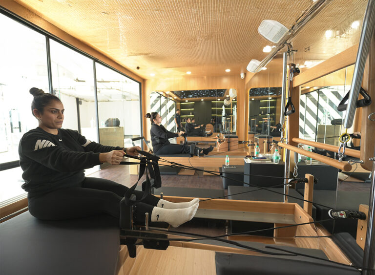 Woman exercising on a Pilates reformer machine in a fitness studio.