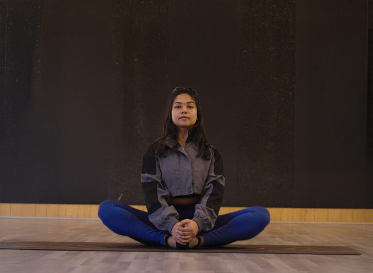“Young woman sitting in a cross-legged yoga pose on a studio floor, practicing mindfulness and relaxation.”