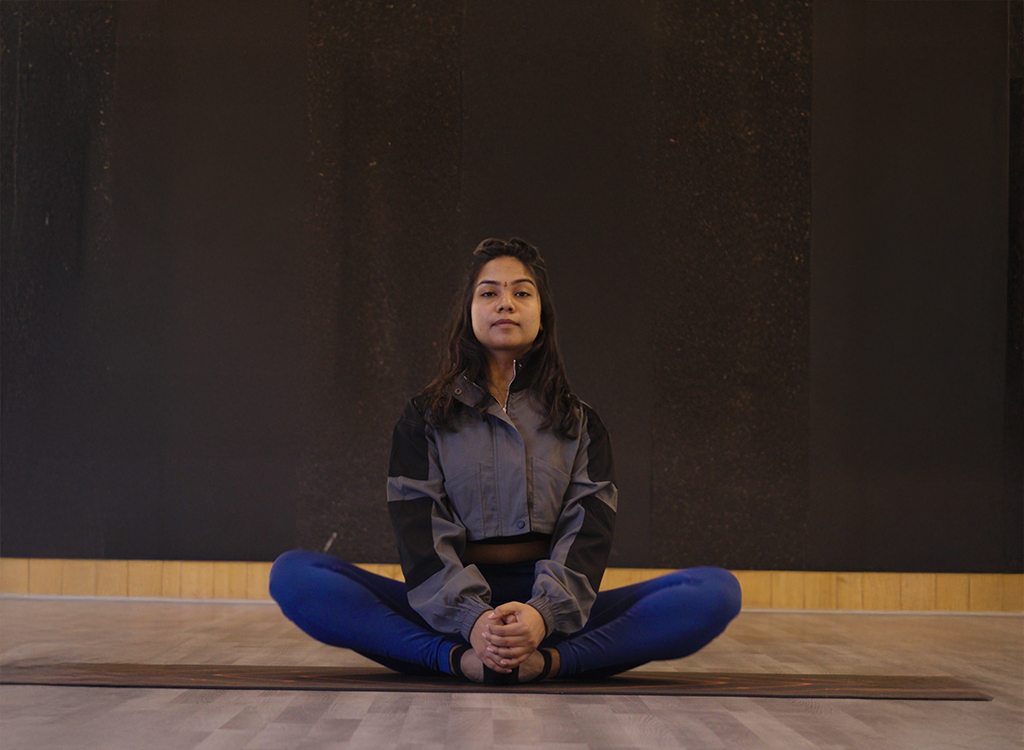 “Young woman sitting in a cross-legged yoga pose on a studio floor, practicing mindfulness and relaxation.”
