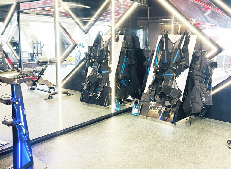 “Fitness studio with EMS training suits hanging on racks beside mirrors and exercise equipment.”