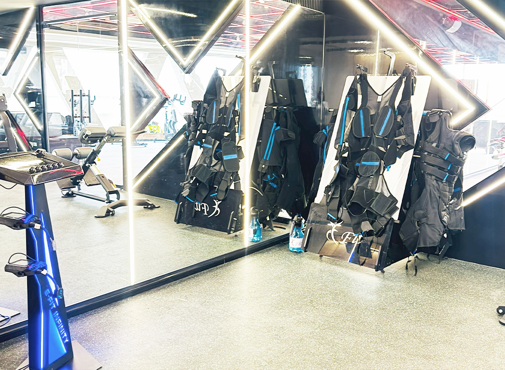 “Fitness studio with EMS training suits hanging on racks beside mirrors and exercise equipment.”