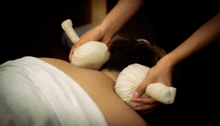 “Therapist performing herbal compress massage on a person’s back.”