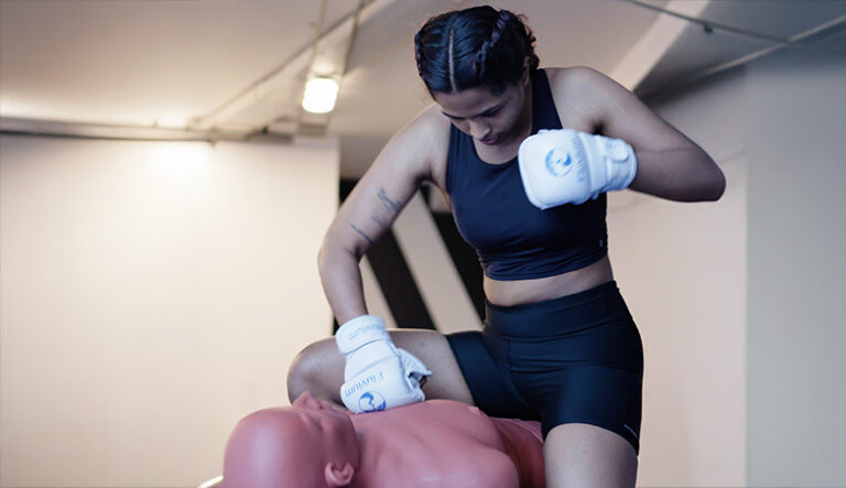 “Woman in sportswear practicing boxing and self-defense techniques on a training dummy.”
