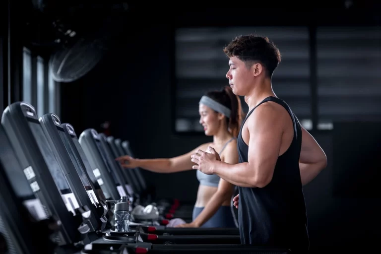 Man and woman running on treadmills in a modern gym during a workout session.